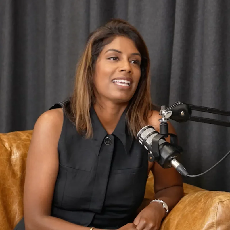 Suji Sanjeevan smiling with Light & Glo candle products in podcast studio